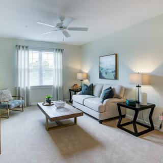 A cozy living room with a comfortable sofa, coffee table, and soft lighting from lamps, featuring a ceiling fan and wall artwork.