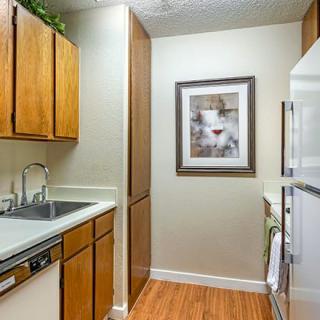A small kitchen with wooden cabinets, a sink, and appliances alongside framed art on the wall.