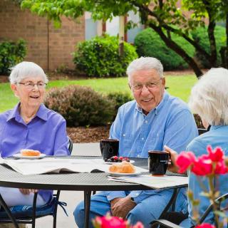 A group of seniors enjoying coffee and conversation outdoors in a garden setting.