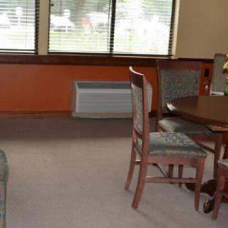 A cozy dining room with a table and chairs, featuring large windows and carpet flooring.