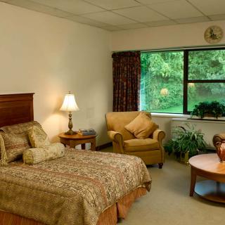 A cozy bedroom with a bed, armchair, and a view of greenery through the window.