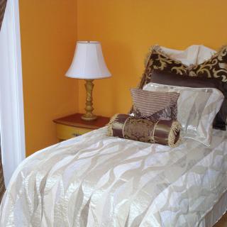 A cozy bedroom corner with a bed adorned with pillows next to an orange wall and a lamp on the nightstand.