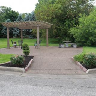 A peaceful park setting with a pergola and outdoor seating surrounded by lush greenery.