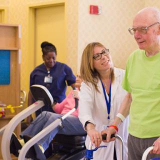 Healthcare professionals assist an elderly man with physical therapy exercises in a rehabilitation setting.