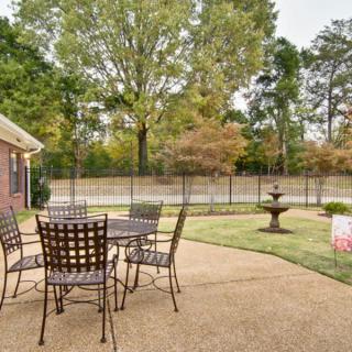 A serene patio area with outdoor furniture overlooking a garden with trees and a fountain.