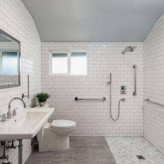 Modern accessible bathroom with white tiles and a walk-in shower.