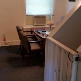 A small office setting with a desk and two chairs near a window with an air conditioner.