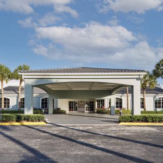 A modern building entrance with palm trees and a partly cloudy sky.