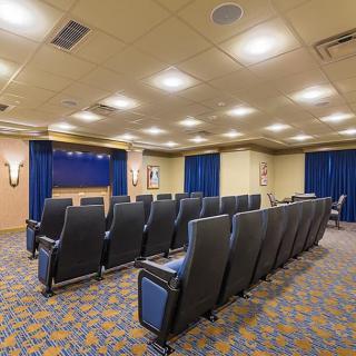 A well-lit theater-style room with rows of comfortable seating facing a projector screen.