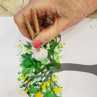 A hand using a paintbrush to create a colorful tree artwork.