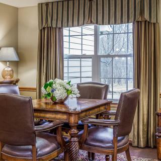 A cozy dining room with a wooden table and leather chairs, adorned with flowers, and illuminated by natural light through the window.