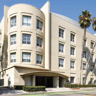 A modern four-story building with large windows, surrounded by palm trees.