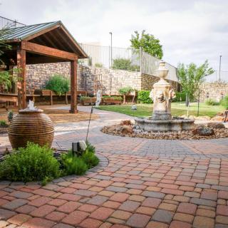 A serene garden courtyard with a central fountain, surrounded by lush greenery and a paved walkway.
