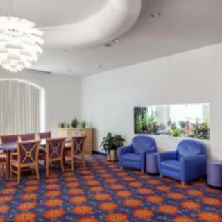A modern room with a dining area and blue armchairs, featuring unique lighting and vibrant carpeting.