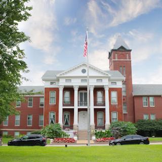 A historic building featuring classic architecture, flanked by well-maintained landscaping and parked cars.