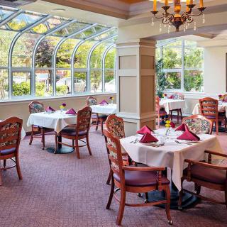 An elegant restaurant dining area with tables set beneath large windows and a chandelier.