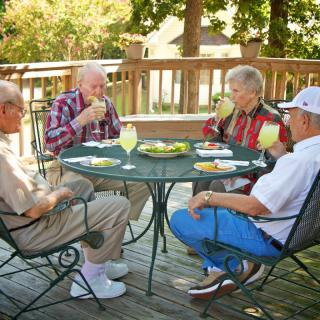 A group of elderly friends enjoying drinks together on a sunny deck.