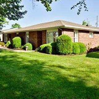 A brick house with a well-maintained lawn and surrounding shrubbery.
