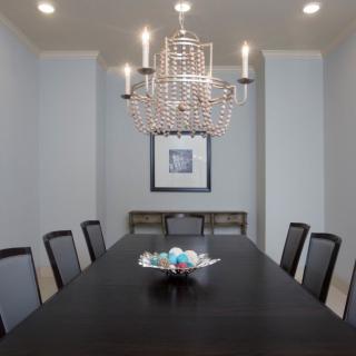 A modern dining room with a large chandelier, featuring a long table and multiple chairs.