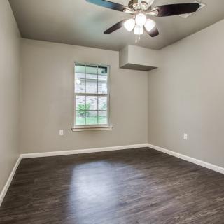 An empty room featuring hardwood flooring, a ceiling fan with lights, and a single window.