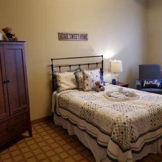 A cozy bedroom with a neatly made bed, bedside lamp, and wooden wardrobe.