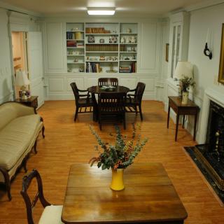 A cozy living room with a dining area, featuring classic wooden furniture and a bookshelf, enhanced by a fireplace.