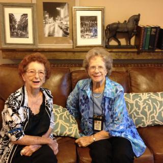 Two women smiling while seated on a couch in a living room.