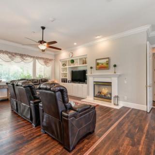 A cozy living room with leather recliners facing a fireplace and television, featuring wooden floors and a ceiling fan.