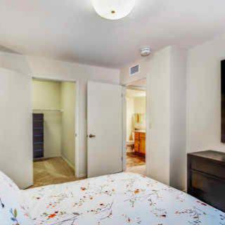 A cozy bedroom featuring a bed with patterned bedding, an open closet, and modern furniture.