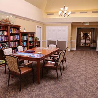 A cozy library space with a central table surrounded by chairs and bookshelves lining the walls.
