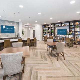 A modern cafe interior with wooden flooring and bookshelves, featuring ample seating and bright lighting.