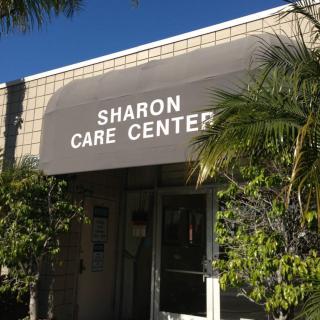Entrance to the Sharon Care Center with a gray awning and surrounding greenery.