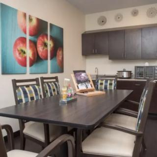 A modern dining area with a dark wooden table, cushioned chairs, and vibrant tomato wall art.