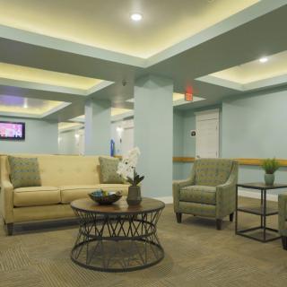 A modern lobby interior featuring comfortable seating with sofas and chairs around a central coffee table under ambient lighting.