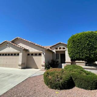 A suburban house with a well-maintained front yard featuring shrubs and a large tree.