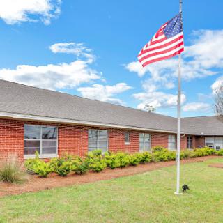 An American flag waves in front of a brick building under a bright blue sky.