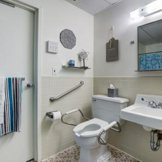 A modern bathroom equipped with a toilet, sink, mirror, and safety handrails.