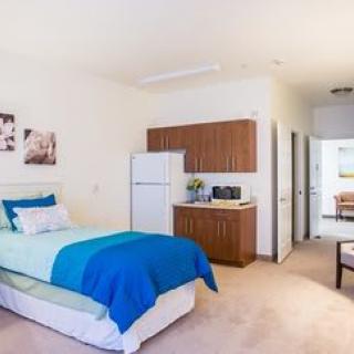 A modern studio apartment interior featuring a cozy single bed and a kitchenette.