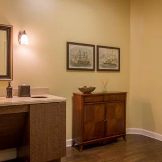 A warmly lit bathroom featuring a wooden cabinet, artwork on the wall, and a countertop with a mirror and light fixture.