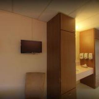 A cozy hotel room featuring a mounted television, wardrobe, and a well-lit sink area with towels.