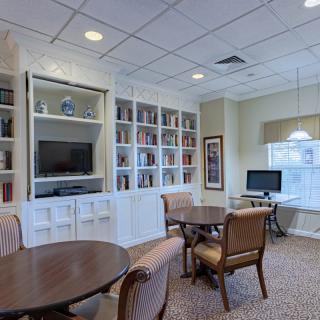A cozy library room with bookshelves, tables, chairs, a computer station, and a television.
