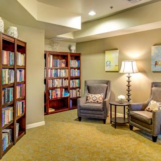 A cozy library corner with bookshelves, armchairs, and a lamp for reading.