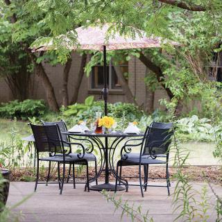 A peaceful patio setting with a table and chairs under an umbrella surrounded by lush greenery.