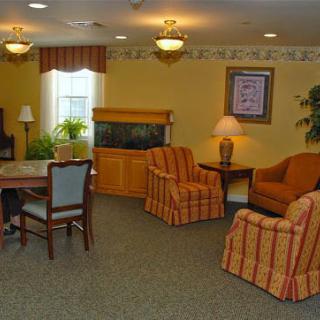 A cozy living room with comfortable chairs, a table, an aquarium, and decorative plants.