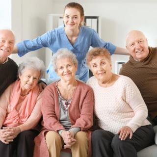 A group of elderly people posing with a caregiver, all smiling in a cozy indoor setting.