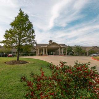 A picturesque building surrounded by landscaped gardens and a wide driveway under a cloudy sky.