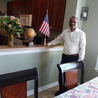 A man standing in a dining area next to an American flag.