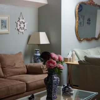 A cozy living room with a sofa, decorative mirror, and floral arrangement.