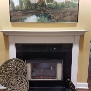 A cozy living room scene featuring a fireplace, elegant decorations, and a landscape painting above the mantel.