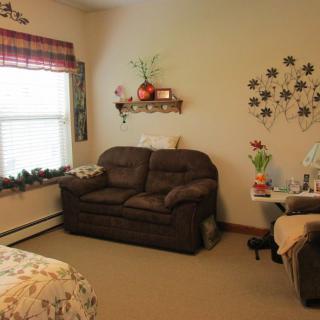 A cozy living room with a brown sofa, decorative wall art, and a shelf adorned with plants.